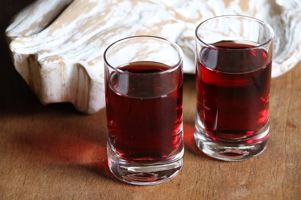 Liqueur glasses with deep red sloe gin in front of a French country-style limed wood...something. An angel's wing or a large sea shell perhaps?